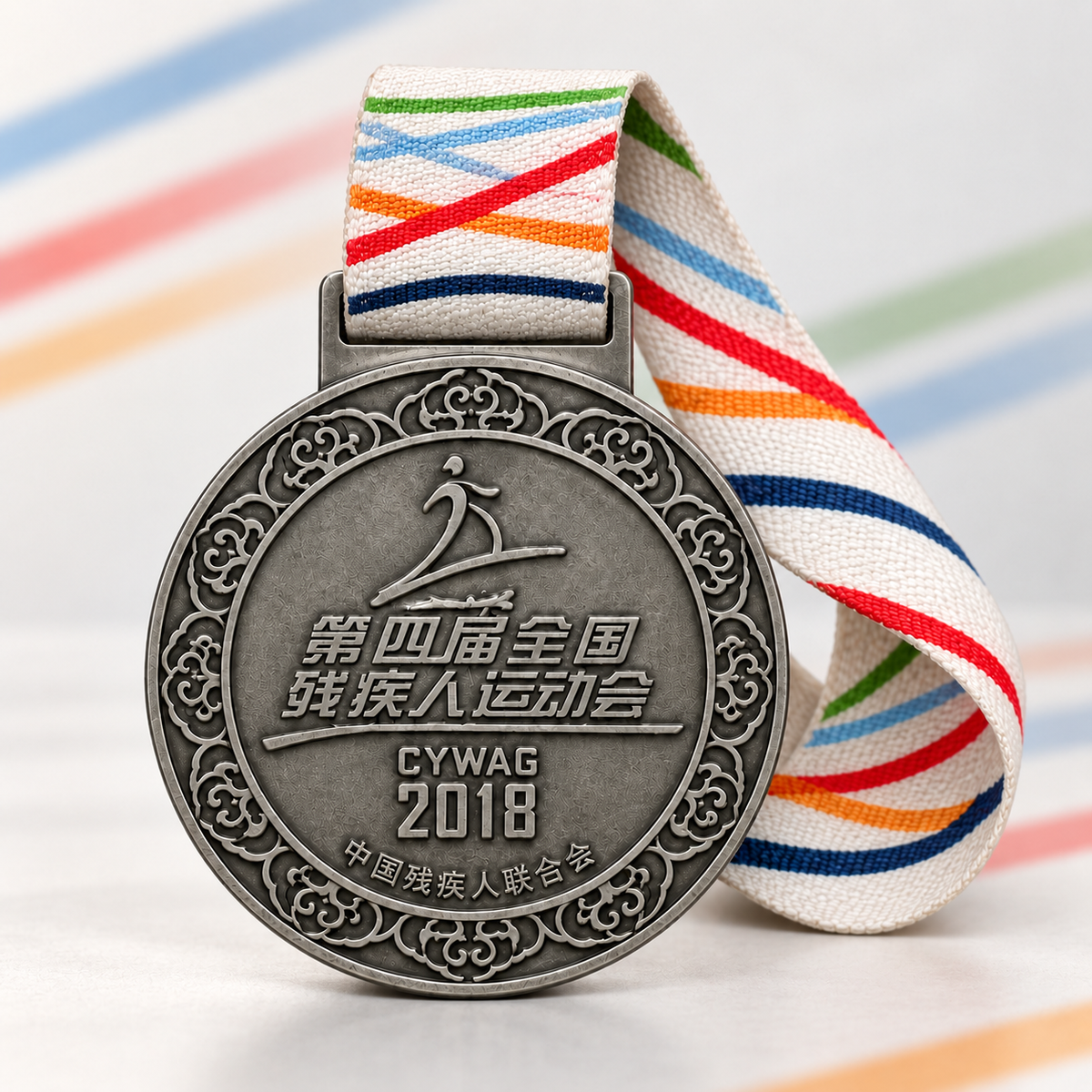 Round dark silver-tone 2018 sports medal with Chinese lettering, a patterned border, and a multicolored striped ribbon