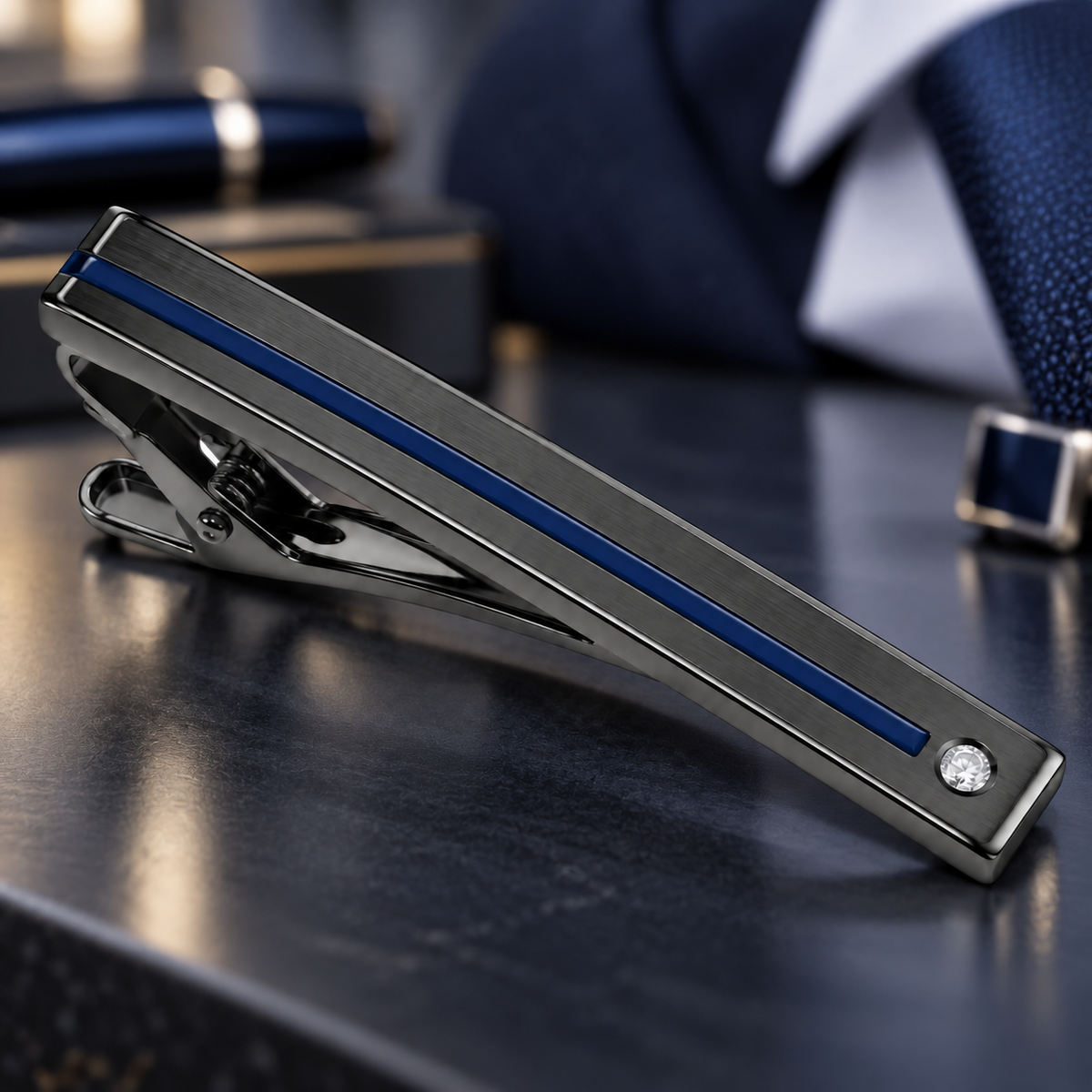 Dark metal tie clip with a narrow blue stripe and a small clear stone at one end