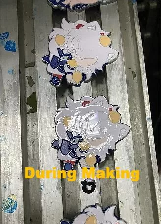 Mid-production stage of enamel pin making, showcasing silk-screen printing alignment and enamel baking process.

